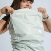 Frau zieht an einer weißen FOLIENMAILER® Versandtasche, um die Festigkeit der Folie zu zeigen