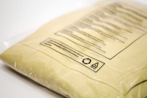 Beiger Pullover in einer ECOBAGS® Textilverpackung mit Warnhinweis-Aufdruck